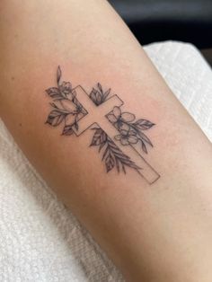 a cross tattoo on the arm with flowers and leaves around it, in black ink