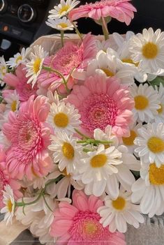 pink and white daisies in a vase on the dashboard of a car or truck