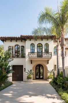 a large white house with lots of windows and palm trees in front of the entrance