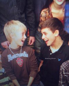 two young boys sitting next to each other in front of a group of people and smiling