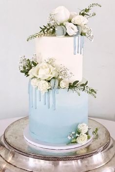 a blue and white wedding cake with flowers on top