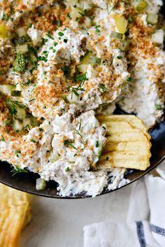 a black bowl filled with potato salad and crackers on top of a white table cloth