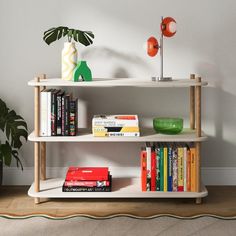 a book shelf with books, vases and other items on it in front of a white wall