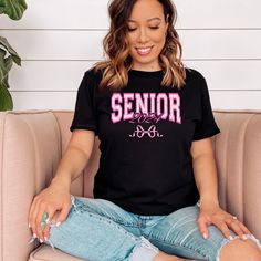 Introducing the "Senior 2024" T-Shirt: the ultimate fashion statement for celebrating the end of your high school journey and the exciting start of a new adventure. Crafted with care, this stylish black T-shirt boasts a charming pink bow, adding a girly, coquette touch to your senior year wardrobe. Perfect for graduation photos, senior parties, and everyday wear, this T-shirt is not just a piece of clothing—it's a keepsake of your achievements and memories. Made from high-quality, soft fabric, i Black Text Print Top For Back To School, Black School Spirit T-shirt With Slogan, Black Collegiate Style Tops For Campus, Black Top With School Spirit For Back To School, Black Tops With School Spirit For Back To School, Black Tops For Back To School With School Spirit, Black T-shirt For College, Back To School, Black Tops For College End Of School Year, Casual Black Tops For College Events