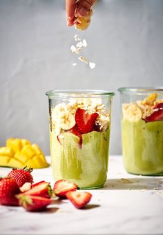 two glasses filled with green smoothie and topped with strawberries