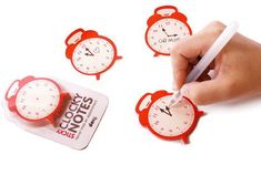 a hand writing on three red clocks with white numbers in front of it and another person's hand holding a pen