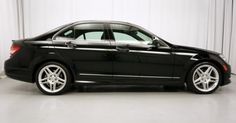 a black car parked in front of a white wall with curtains on the back side