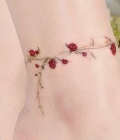 a rose tattoo on the side of a woman's leg, with red flowers growing out of it