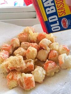 a box of old bay bread sitting on top of a white napkin next to a pile of fried food