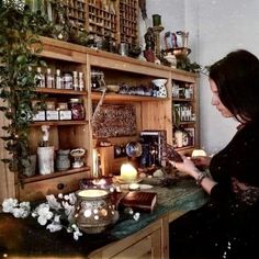 a woman sitting at a table in front of a shelf filled with jars and candles