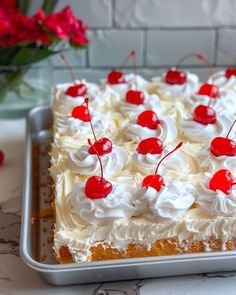 a square cake with white frosting and cherries on top is sitting on a table