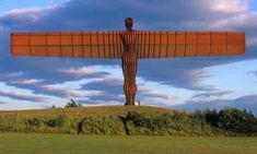 a large metal angel standing on top of a lush green field under a blue cloudy sky