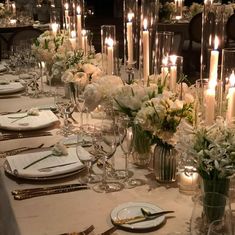 a long table is set with white flowers and candles for an elegant dinner or party