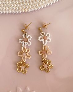 Our Beaded Pastel Flower Drop Earrings are a delightful and charming addition to your jewelry collection. They feature a cascade of delicate pastel-hued beads intricately arranged in the form of flowers, creating a playful and feminine design. The beaded flowers gently dangle, adding subtle movement and a touch of whimsy to your look. Whether you are dressing up for a special event or adding a touch of color to your everyday style, they are a versatile and eye-catching accessory. Details & Care Handmade Feminine Flower Shaped Earrings, Handmade Feminine Flower Earrings, Handmade Feminine Flower-shaped Earrings, Dainty Handmade Flower Earrings, Handmade Cream Flower Earrings, White Beaded Flower-shaped Earrings For Gifts, Dainty White Beaded Earrings For Gifts, Flower Drop Earrings, Drop Earrings Gold