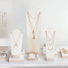 several necklaces and rings are displayed on a white table with wooden stand for display