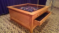 a wooden box with glass top and drawers on the floor in front of a curtained wall