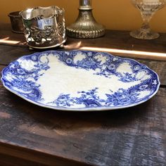 a blue and white plate sitting on top of a wooden table next to silver cups