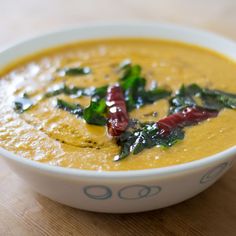 a white bowl filled with yellow soup on top of a wooden table