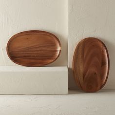 two wooden plates sitting next to each other on top of a white block in front of a wall