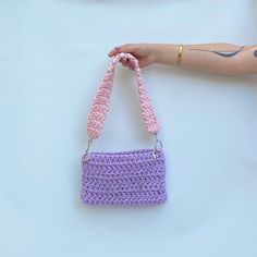 a hand holding a purple crocheted purse with a pink handle and chain attached to it