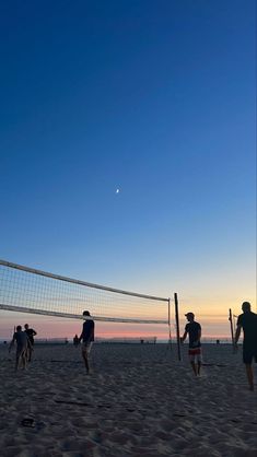 people playing volleyball on the beach at sunset