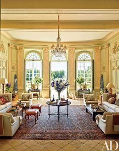 a living room filled with lots of furniture next to two large windows and a chandelier