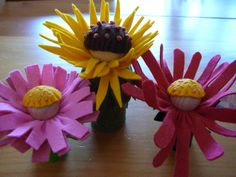 three fake flowers are sitting in a vase on the table, one is pink and yellow