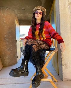 a woman sitting on top of a step ladder wearing black boots and a red sweater