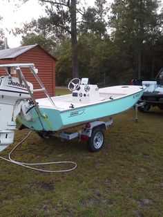 a blue and white boat parked next to a red barn with two other boats in the yard