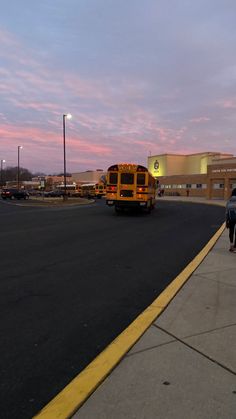 a yellow school bus driving down a street next to a parking lot with cars parked in front of it