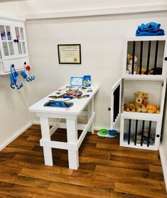 there is a table with stuffed animals on it in the room that has white walls and wooden floors