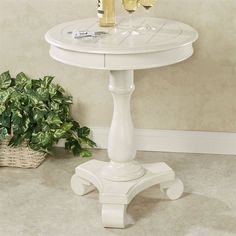 a white table with two glasses of wine on it next to a potted plant