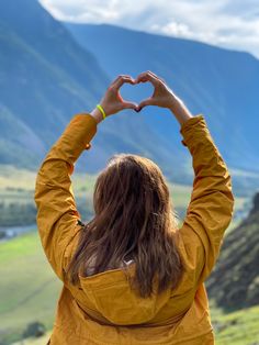 a woman with her hands in the shape of a heart on top of a mountain