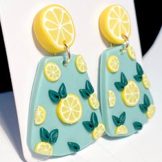 a pair of earrings with lemons and leaves painted on the outside, hanging from hooks