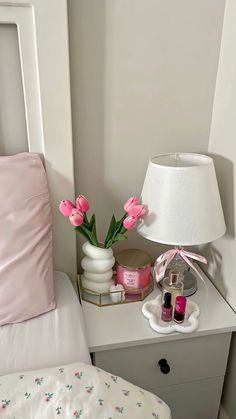 a white nightstand topped with pink flowers next to a bed