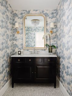 a bathroom with blue and white wallpaper has a large mirror above the sink, along with two lamps on either side of the vanity