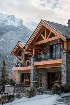 a large stone and wood house in the mountains with snow on the ground around it