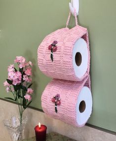 two rolls of toilet paper are hanging on the wall next to a vase with flowers