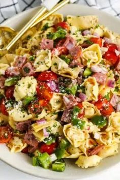 pasta salad with ham, tomatoes, and green peppers in a white bowl on a table