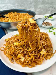 a white plate topped with noodles next to a pan filled with rice and other food