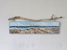 a piece of wood hanging on a wall next to a branch with water and sand painted on it