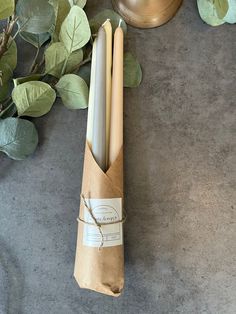 two candles are wrapped in brown paper and tied with twine on the table next to some green leaves