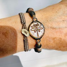 Unique Glass Dragonfly connector sits with African Recycled Glass beads in black and mottled brown. This bracelet is sized for the small wrist at 7 inches in length. Read below to determine you sizing. To ensure the desired fit of bracelets: Measure your wrist and add 1/2 to 3/4 inch. Think about where you want the particular bracelet to hang - snug, a bit loose or looser to wear lower on your hand.  Example: my wrist measures 6.75" in length  A 7" length  is tight but wearable A 7.25" length is the size I prefer  A 7.50" length is doable, a bit looser but still wearable  To see all my unique handmade jewelry visit www.majidesigns.etsy.com Shipping is FREE in the USA! My turnaround time is 1-2 days. I ship 1st class mail.  Any additional questions:  Majidesignsjewelry@gmail.com Adjustable Nickel Free Artisan Bracelets, Adjustable Earthy Jewelry For Friendship, Nature-inspired Adjustable Beaded Bracelet With Round Beads, Nickel-free Adjustable Dragonfly Jewelry, Adjustable Nature-inspired Bracelet With Round Beads, Adjustable Beaded Nature-inspired Bracelet, Adjustable Nature-inspired Jewelry With Round Beads, Nature-inspired Adjustable Hand-strung Jewelry, Handmade Adjustable Round Wrap Bracelet