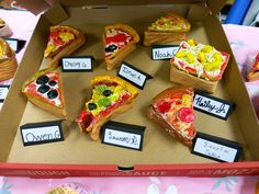 a box filled with different kinds of pizzas on top of a table next to cupcakes