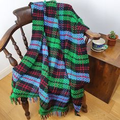 a chair with a blanket on top of it next to a wooden table and potted plant