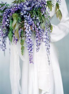 a woman wearing a white dress holding a bouquet of purple flowers in her hands and the back of her body