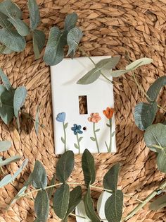 a white house surrounded by green leaves and flowers on a wicker table with a light switch