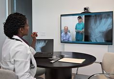 a woman sitting at a table in front of a laptop computer with an x - ray image on the wall behind her