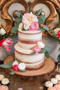 a three tiered cake with flowers and greenery sits on top of a wood slice