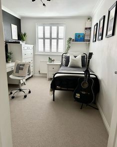 a bedroom with a bed, desk and guitar on the floor next to a window